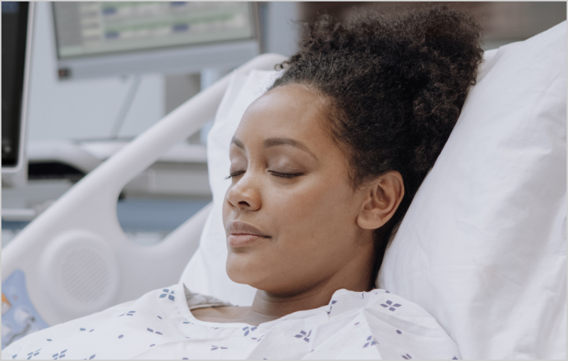 Patient à la peau sombre sur un lit d'hôpital surveillé par un dispositif Masimo Root.