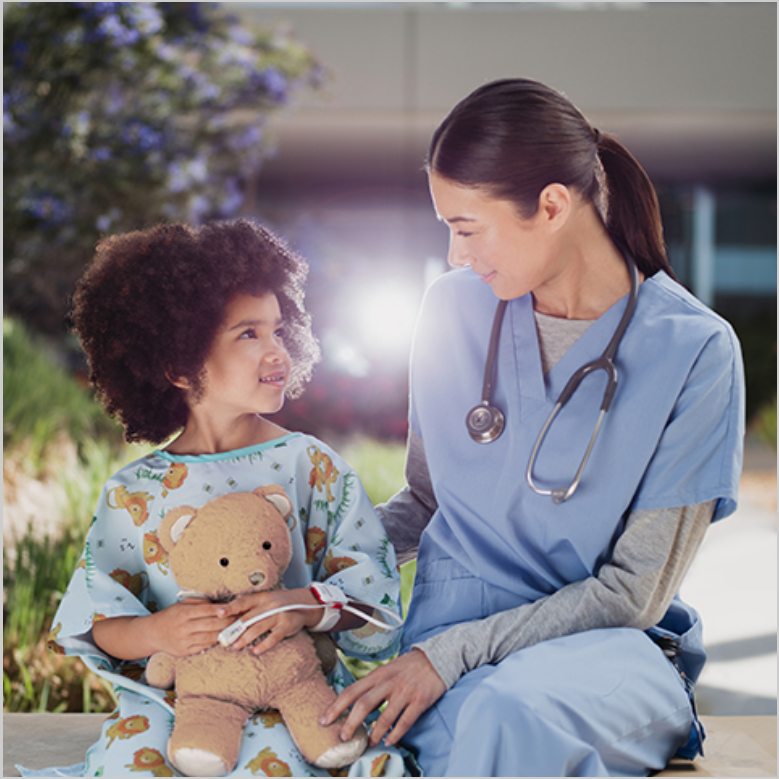 Clinicien portant un stéthoscope assis dehors avec un enfant tenant un ours en peluche et portant un capteur Masimo. 